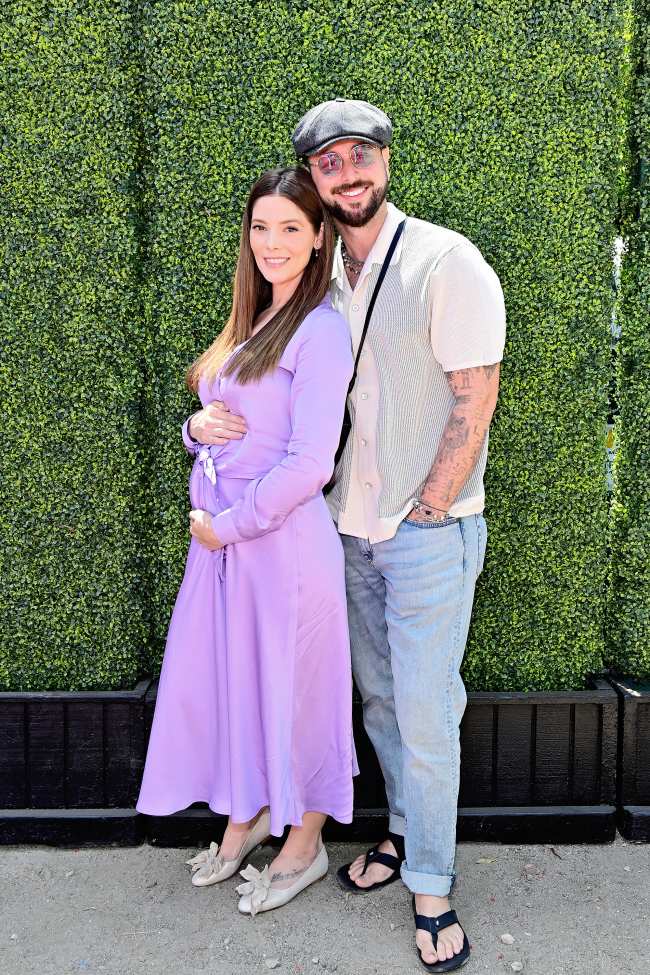 Ashley Greene y Paul Khoury embarazadas posan frente a un muro de cesped