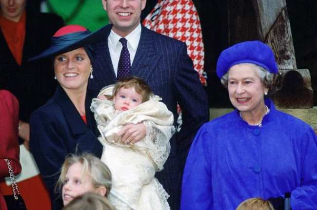Sarah Ferguson cargando a un bebe de pie junto a la Reina