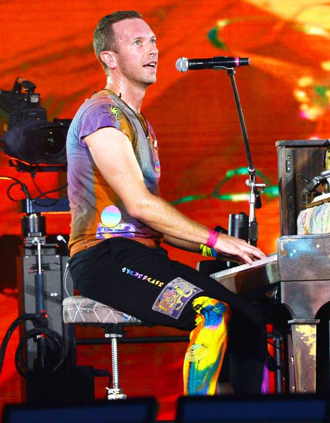 Chris Martin de Coldplay sentado en un piano interpretando