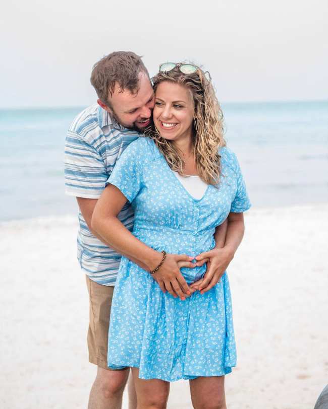 John David Duggar abrazando a la embarazada Abbie Burnett por detras en una playa