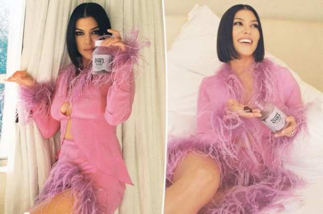 Kourtney Kardashian con un traje de plumas rosas sosteniendo un envase de vitaminas