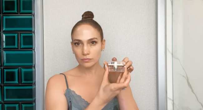 Jennifer Lopez con una camisola de encaje gris sujetando el contorno de ojos