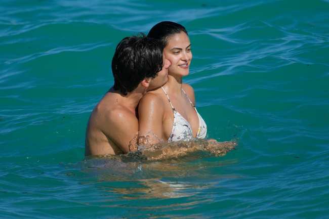 Rudy Mancuso abrazando a Camila Mendes por detras en un oceano