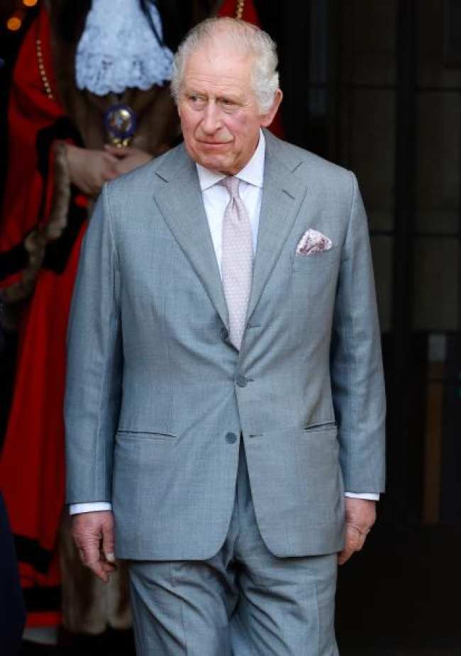 El rey Carlos esta de pie con un traje gris y una corbata rosa