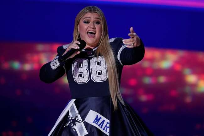 Kelly Clarkson se para en el escenario con un microfono en un vestido de los Dallas Cowboys