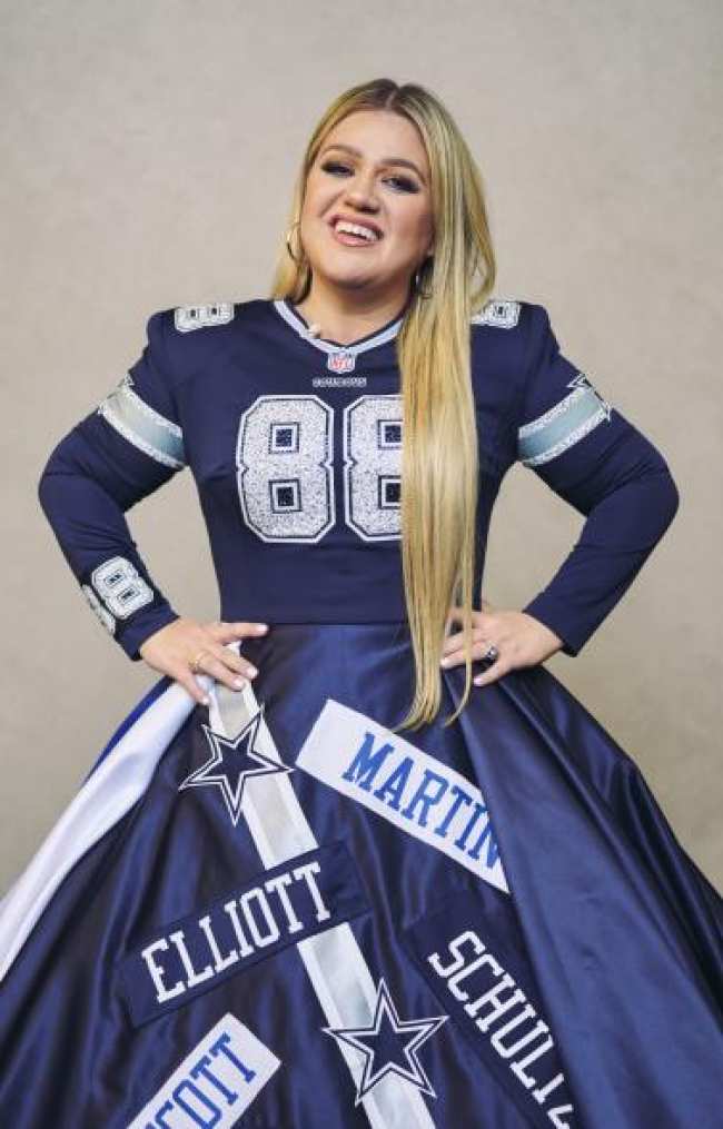 Kelly Clarkson sonrie con las manos en las caderas con un vestido de los Dallas Cowboys