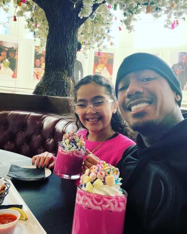 Nick Cannon sonrie en una selfie mientras esta sentado en un puesto de restaurante con su hija Monroe