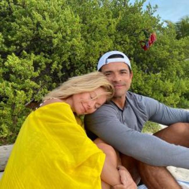 Kelly Ripa apoya su cabeza en Mark Consuelos mientras esta sentada en la playa