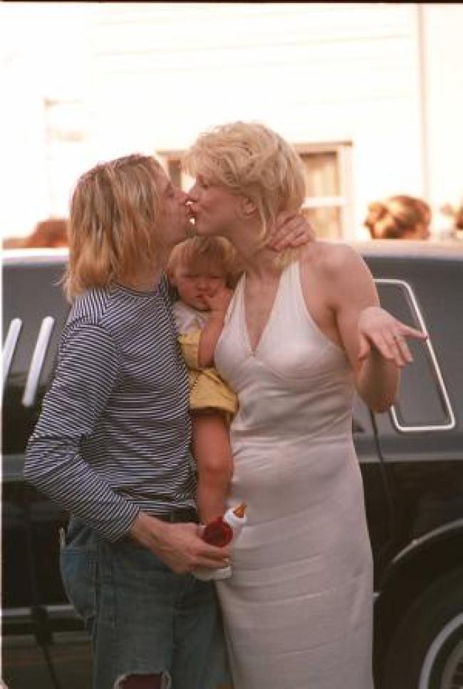Courtney Love y Kurt Cobain besandose con la bebe Frances Bean en el medio