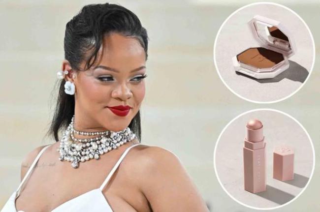 Rihanna con un vestido blanco, observando las inserciones de una base en polvo y un iluminador en barra