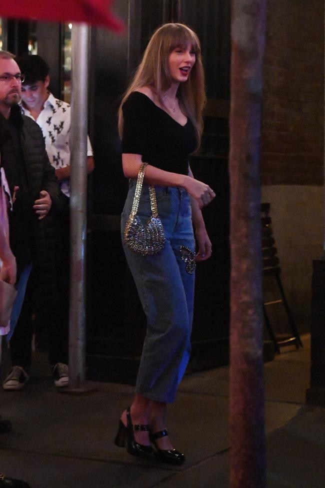 Taylor Swift portando un bolso plateado y vistiendo una camisa negra y jeans