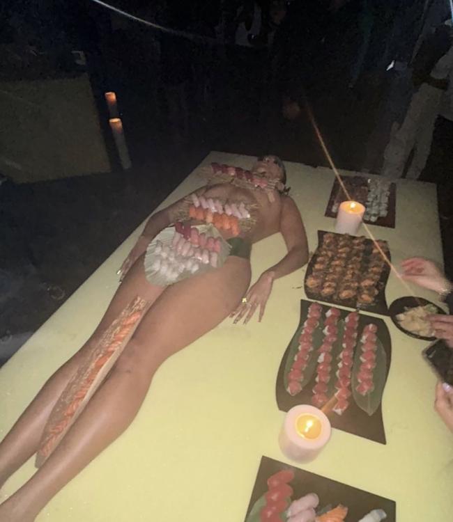 una mujer desnuda acostada en una mesa con sushi cubriéndola