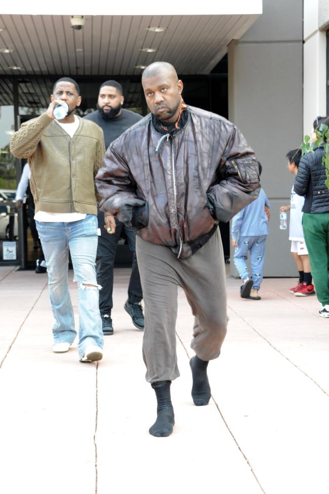 Kanye West caminando con una chaqueta de cuero marrón.
