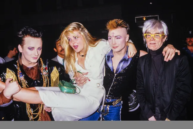 Cornelia siendo llevada por Boy George, Marilyn y Warhol en 1985.
