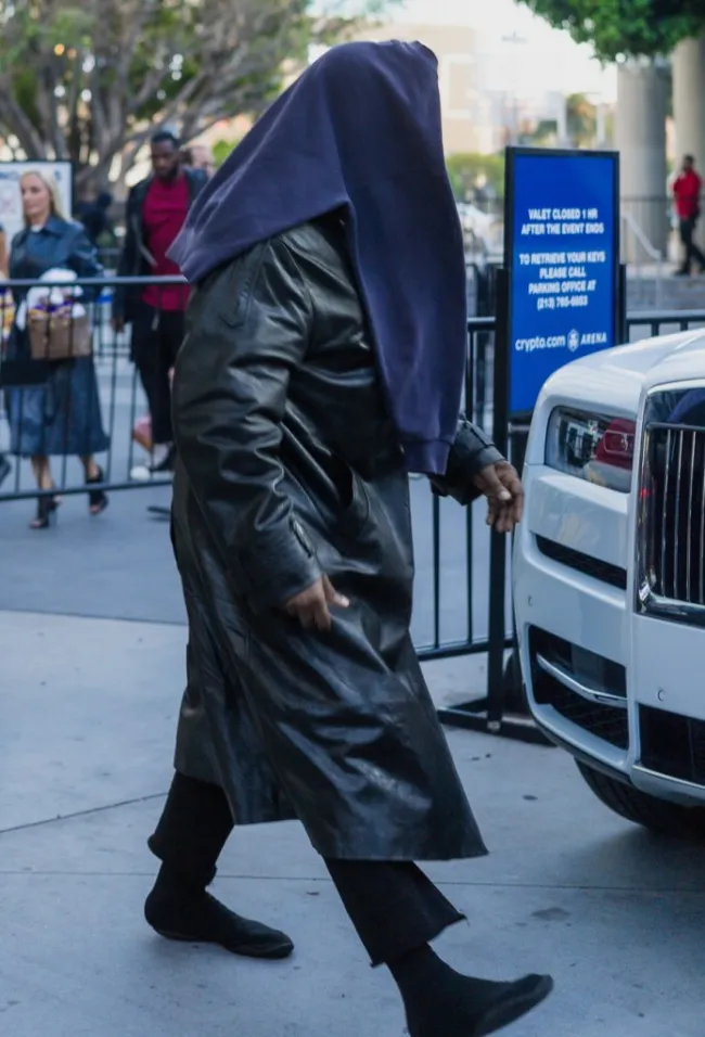 Kanye West caminando con una sudadera en la cabeza.