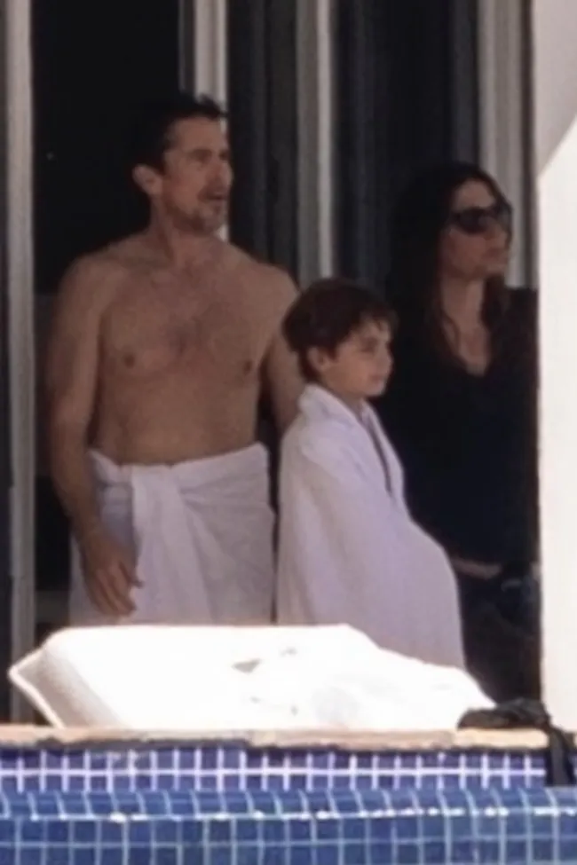 Christian Bale con una toalla en la cintura junto a su hijo.
