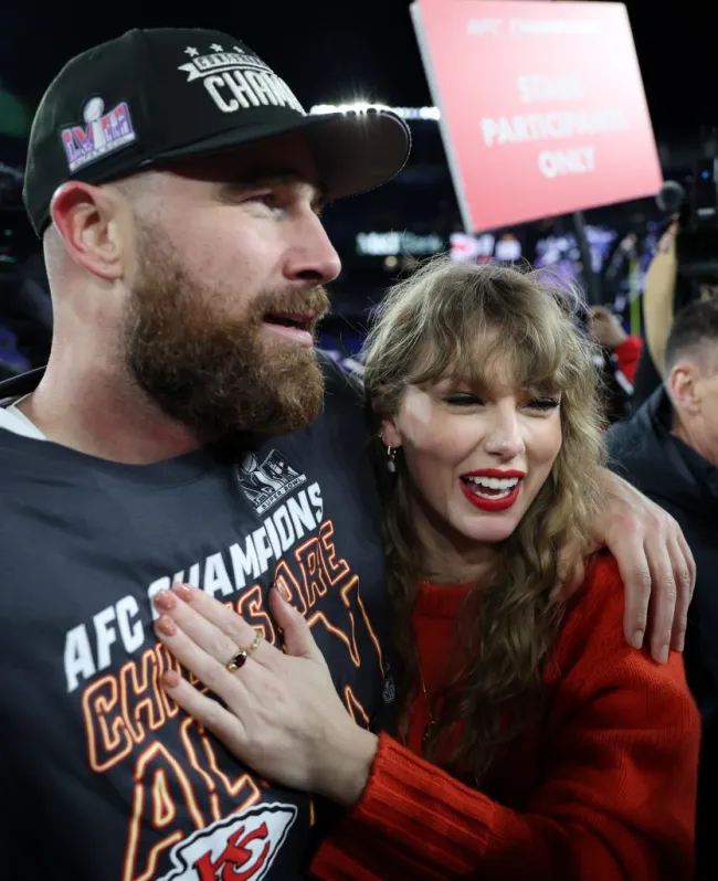 Travis Kelce rodea con su brazo a Taylor Swift, quien tiene su mano en su pecho, en el campo de fútbol.