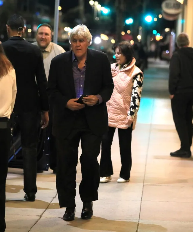 Jay Leno caminando por la calle con su esposa, Mavis, detrás de él.