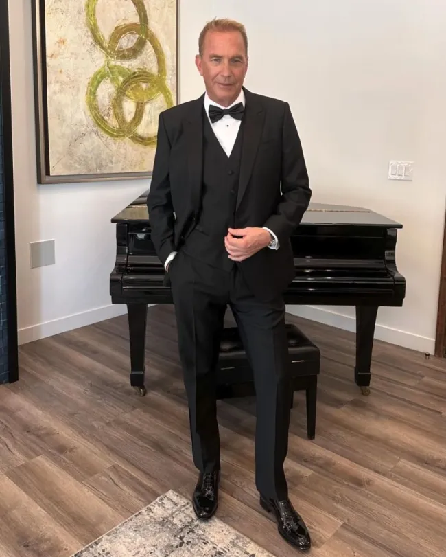 Kevin Costner posando con esmoquin frente a un piano