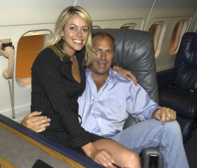 Christine Baumgartner sentada en el regazo de Kevin Costner en un jet