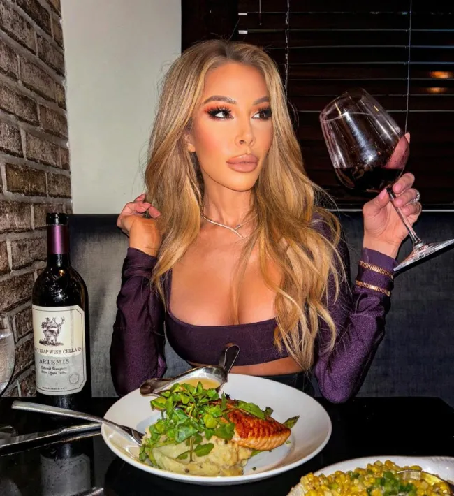 lisa hochstein sosteniendo una copa de vino en la mesa de un restaurante con pescado frente a ella