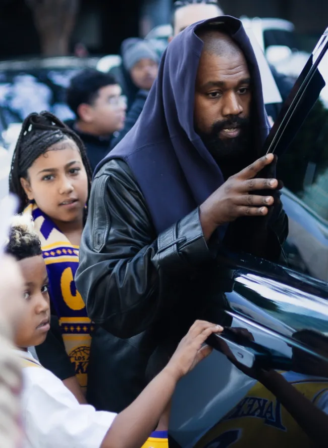 Kanye West subiéndose a un auto con North West y Saint West.