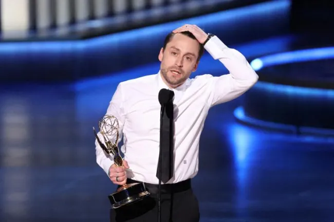 Kieran Culkin en el escenario de los Emmy, con una mano en la cabeza y la otra sosteniendo el premio