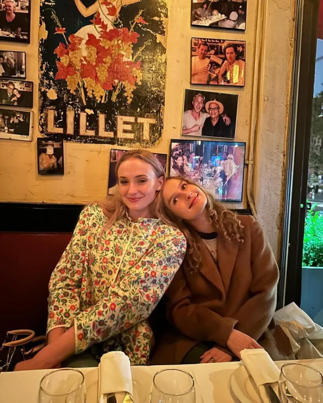 Sophie Turner y una amiga apoyando su cabeza en el hombro de Sophie en la mesa de un restaurante.