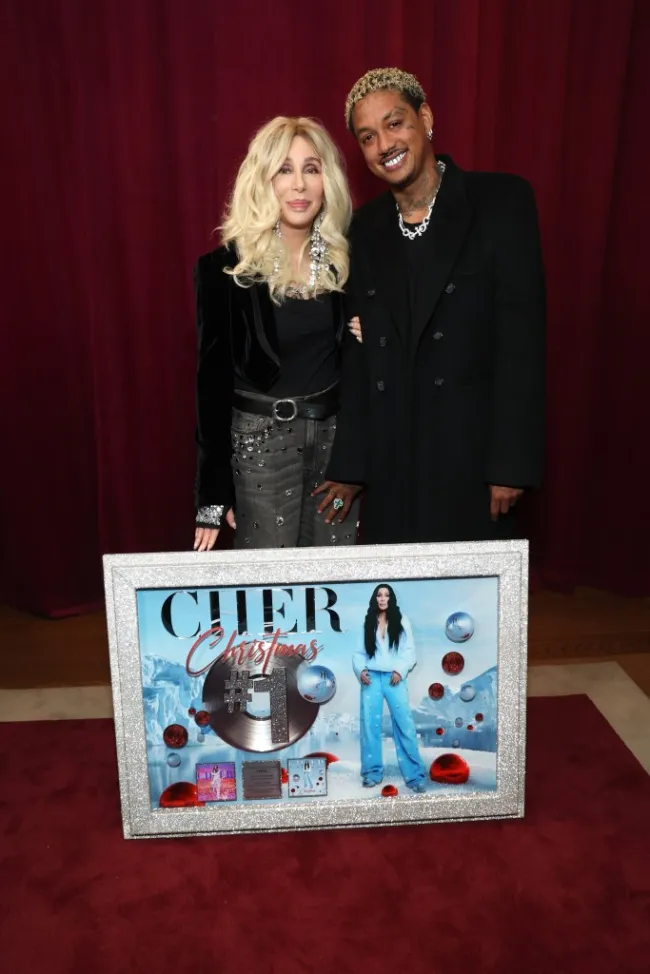 Cher y Alexander Edwards de pie junto a una placa enmarcada de su álbum navideño número uno.