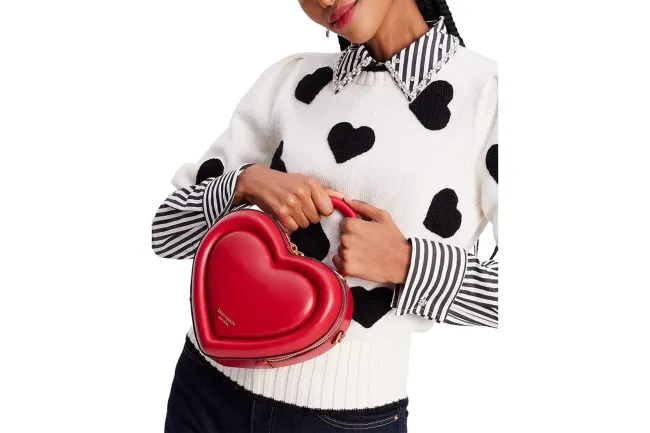 Una modelo con un suéter de corazones sosteniendo un bolso rojo.