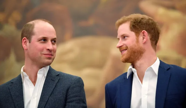 El príncipe William y el príncipe Harry mirándose y sonriendo