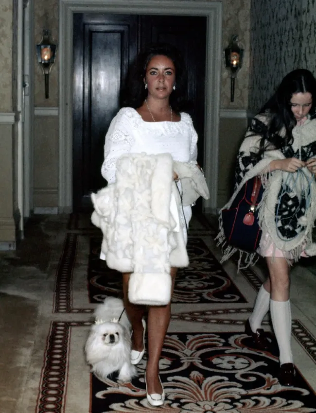 Elizabeth Taylor paseando a un pequeño perro con correa sobre una alfombra estampada