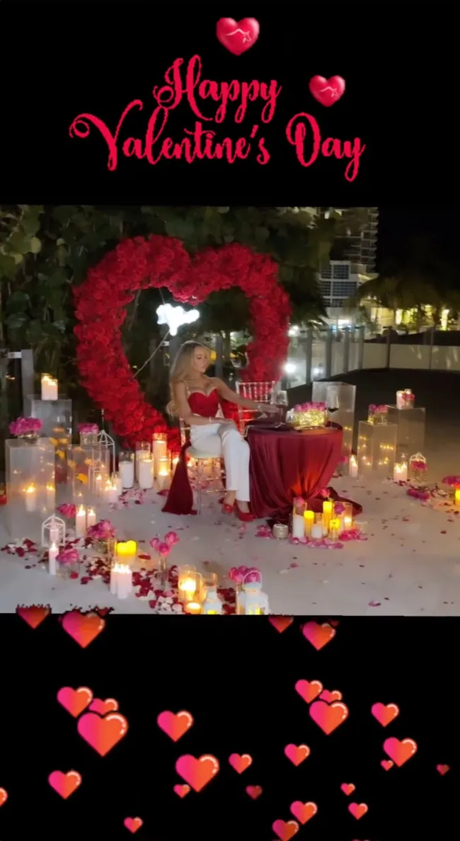 lisa hochstein sentada en una pequeña mesa rodeada de velas, rosas y una corona de rosas en forma de corazón
