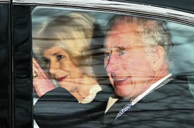 El rey Carlos III saludando dentro de un coche con la reina Camila