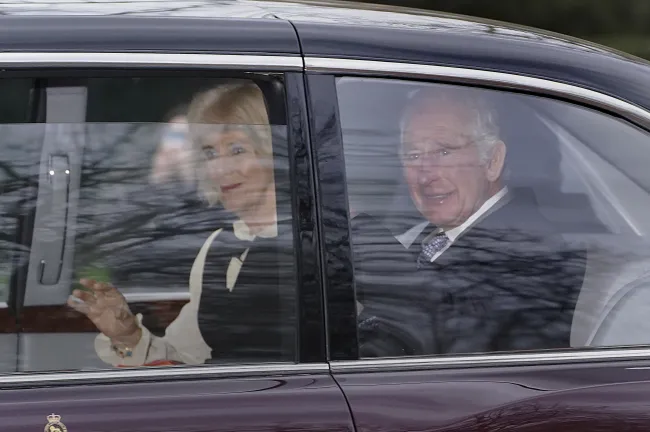 El rey Carlos III saludando dentro de un coche con la reina Camila