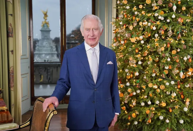 El rey Carlos III de pie frente a un árbol de Navidad con la mano en una silla