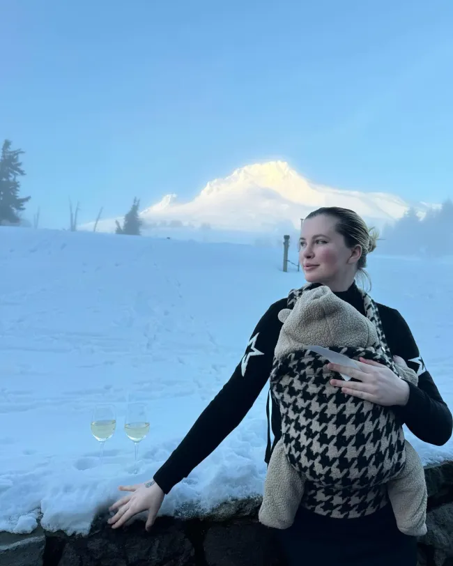Irlanda Baldwin sosteniendo a su bebé en un portabebés rodeada de nieve