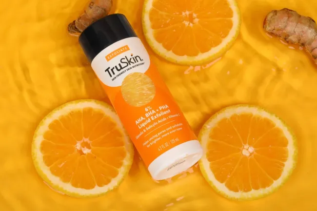Una botella exfoliante en agua rodeada de naranjas.