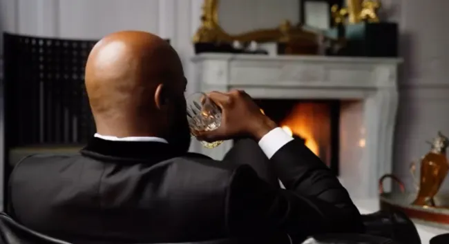 Un hombre bebiendo un cóctel frente a una chimenea en el vídeo de la boda de Cynthia Bailey