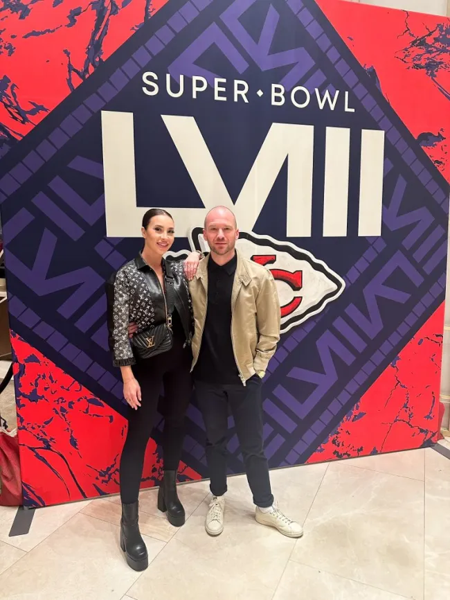 Sean Evans y Melissa Stratton parados frente al mural del Super Bowl Lviii