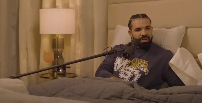 Drake en la cama hablando por un micrófono.