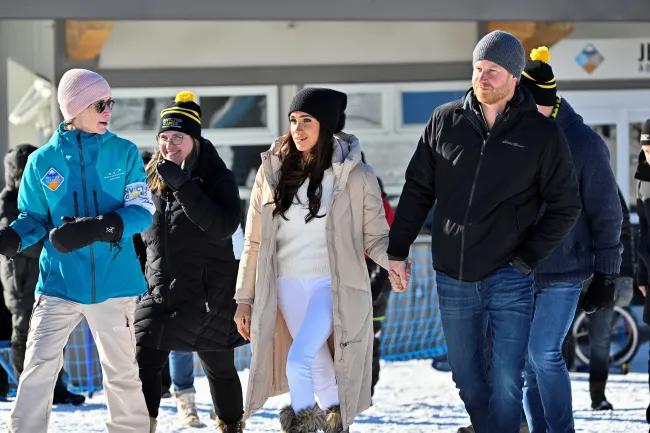 El príncipe Harry y Meghan Markle se dan la mano en un lugar nevado. Ambos llevan sombreros.