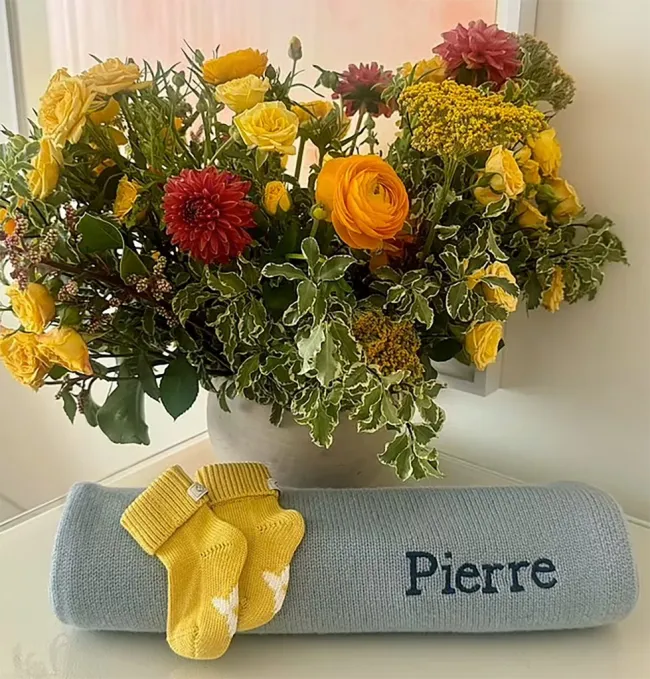 un ramo de flores, una manta enrollada con Pierre bordado y un par de calcetines de bebé