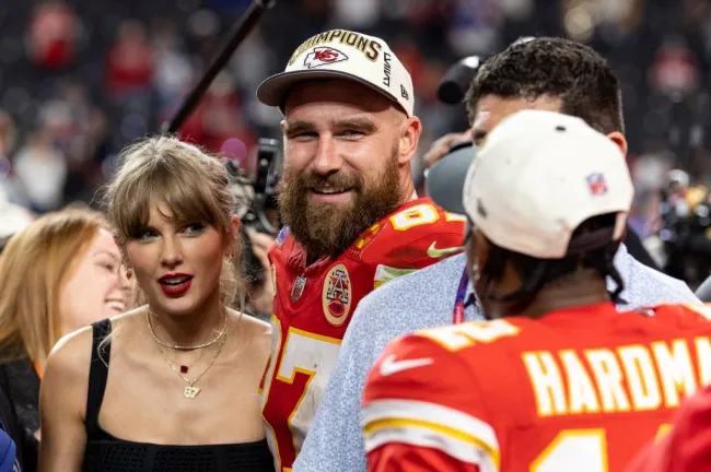 Taylor Swift y Travis Kelce hablando con un jugador de fútbol.