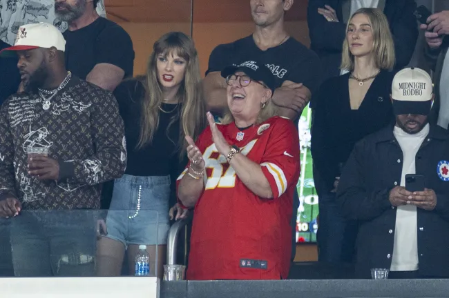 Taylor Swift apoyada en Donna Kelce rodeada de otras personas en un palco en un estadio de fútbol.