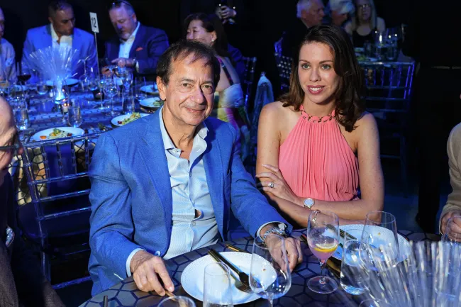 John Paulson y su novia Alina de Almeida sentados en una mesa.