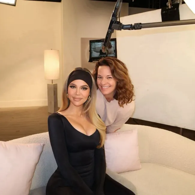 Khloé Kardashian sentada en el sofá sonriendo a la cámara con Erin Paxton detrás de ella