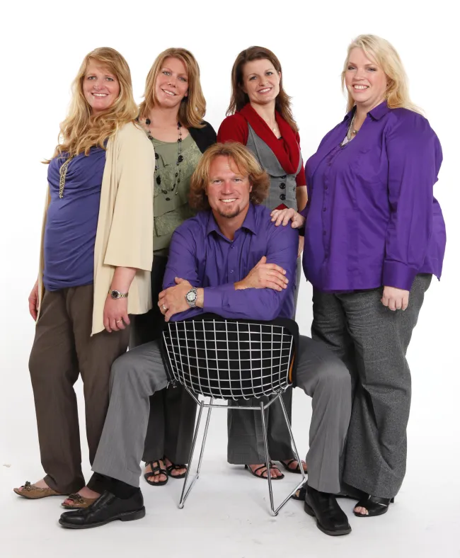 Kody Brown y sus cuatro esposas y sus numerosos hijos.  En esta foto;  Meri (camisa verde, bolero negro), Christine (cárdigan color crema, camisa morada), Kody Brown (hombre con camisa morada), Robyn (camisa roja, chaleco gris) y Janelle (morada)