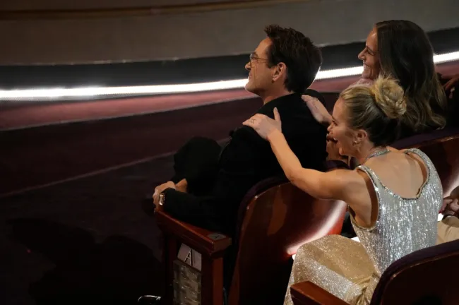 Emily Blunt poniendo sus brazos sobre los hombros de Robert Downey Jr.