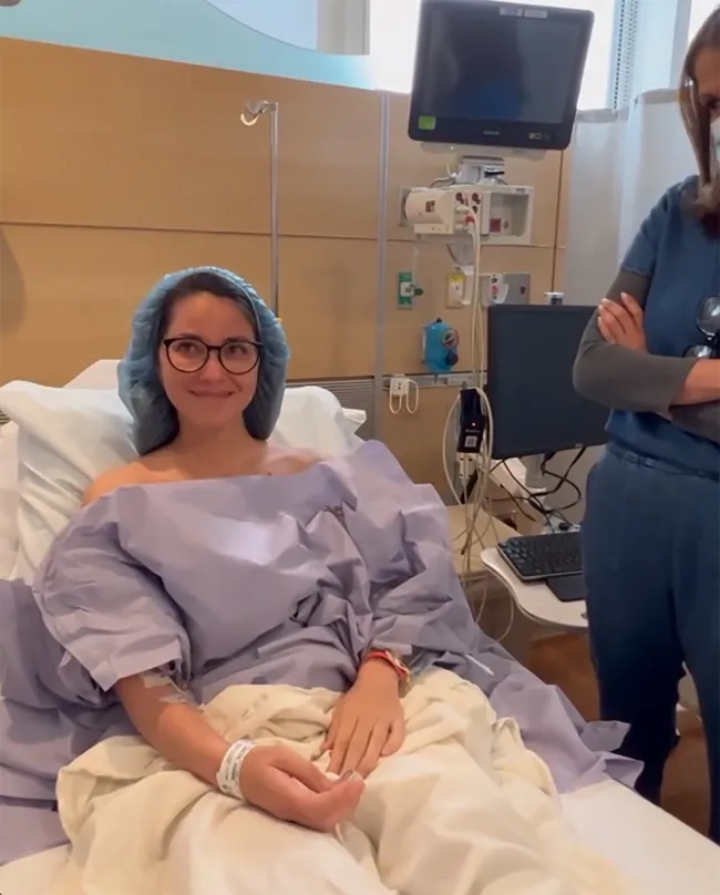 Olivia Munn en bata de hospital y en cama.